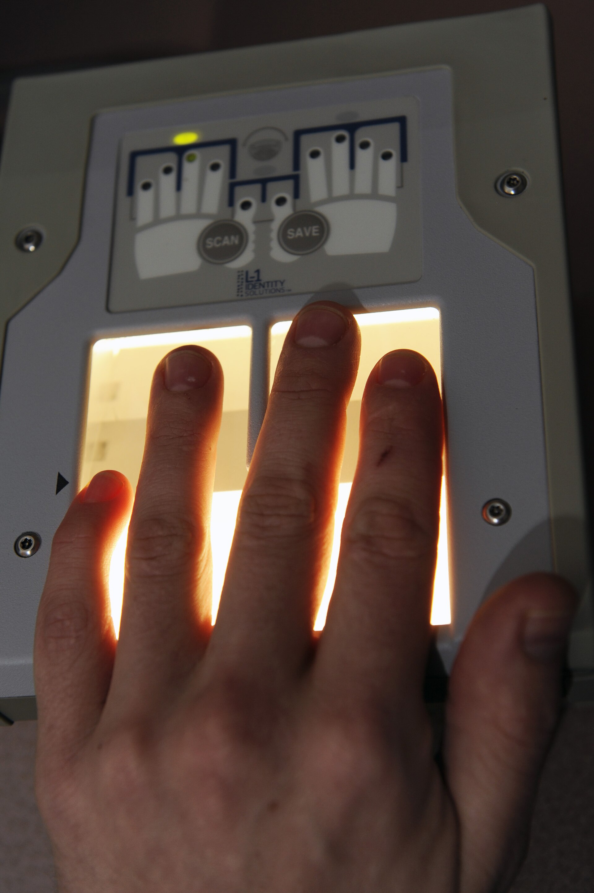 A hand pressed flat on a lit electronic ten-print fingerprint scanner of the kind used for digital fingerprinting.