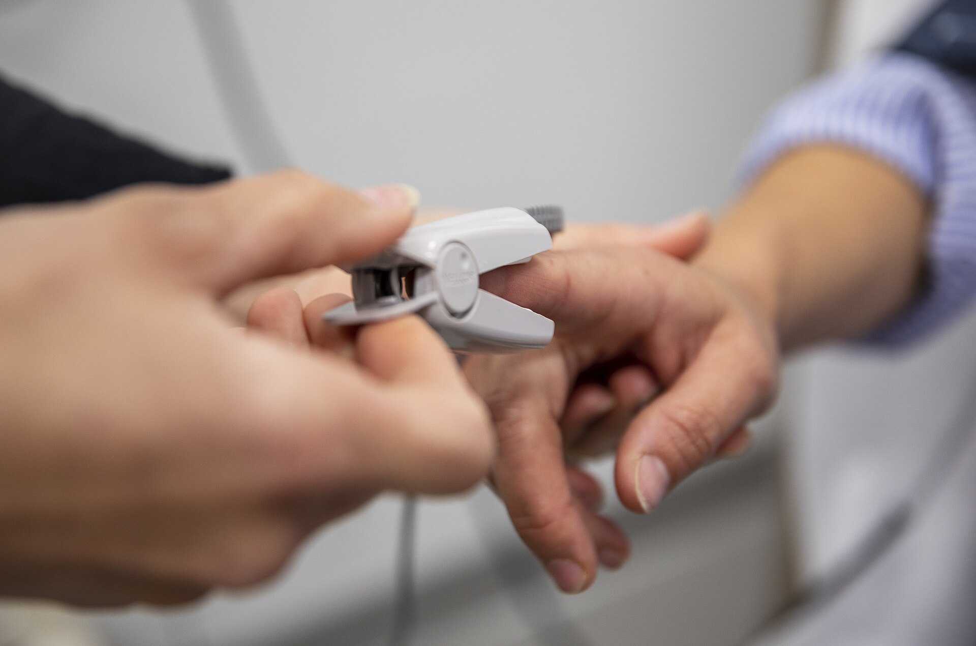 Close-up of a nurse's hands placing a pulse oximeter sensor on a patient's finger.